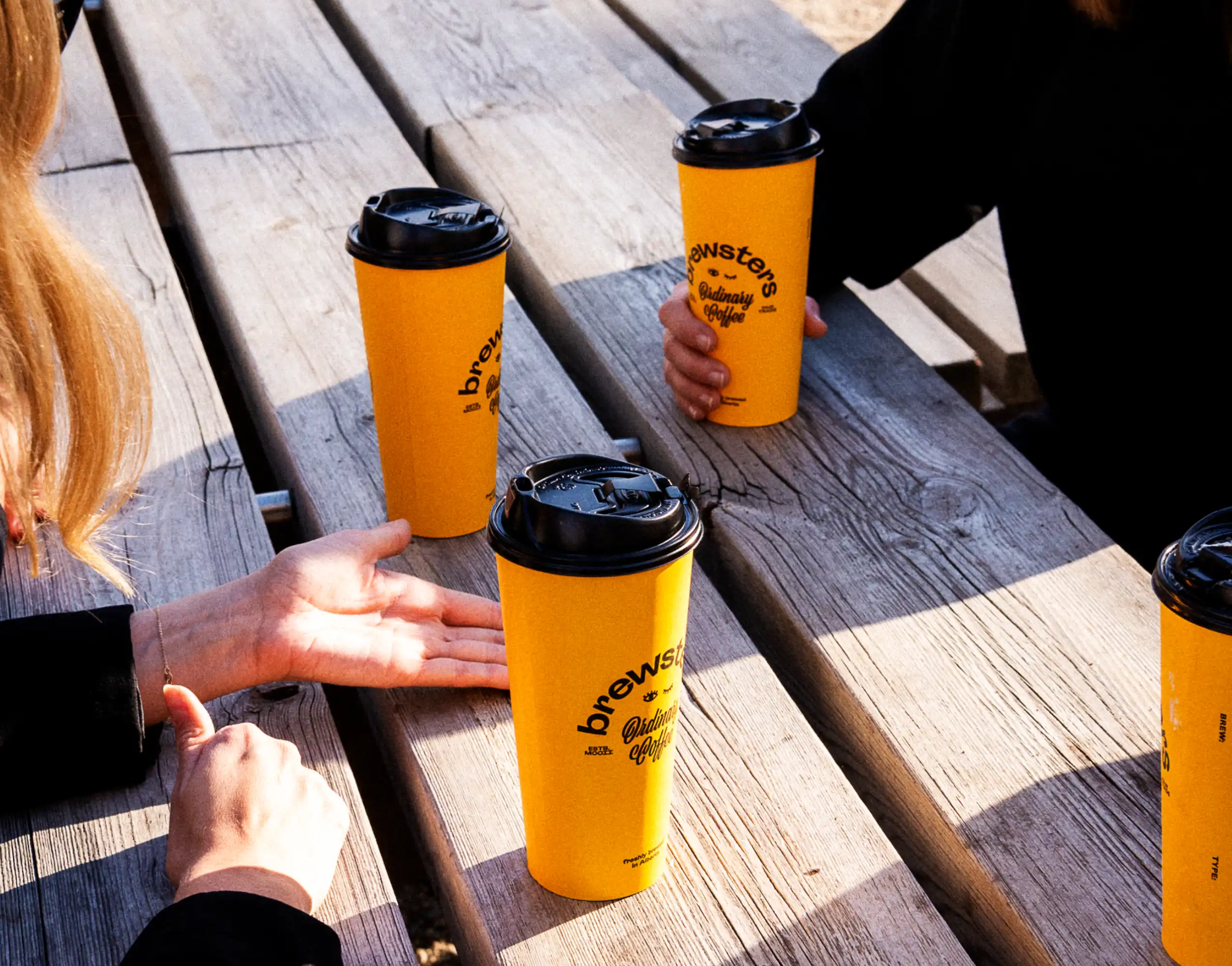 People sitting at picnic bench in park with Brewsters cups